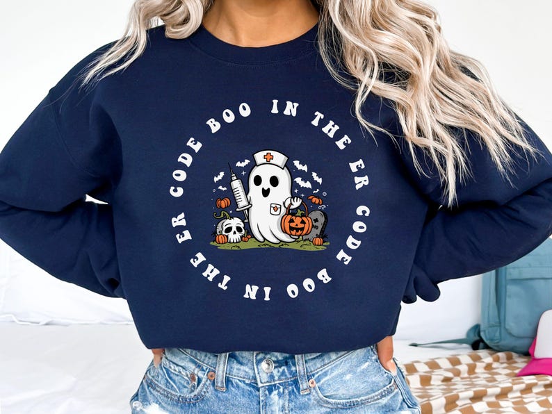 May include: A navy blue sweatshirt with a white graphic of a ghost wearing a nurse's hat and holding a syringe and a pumpkin. The text "Boo in the ER Code Boo in the ER Code" is printed in a circle around the ghost.