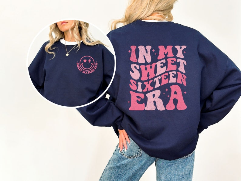 May include: Navy blue sweatshirt with a pink graphic on the back that says "In My Sweet Sixteen Era" and a pink smiley face with a heart and lightning bolt on the front.