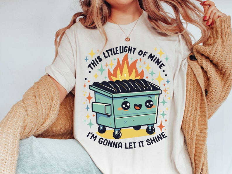 May include: White t-shirt with a graphic of a green dumpster on fire with a smiling face and the text "This little light of mine, I'm gonna let it shine."