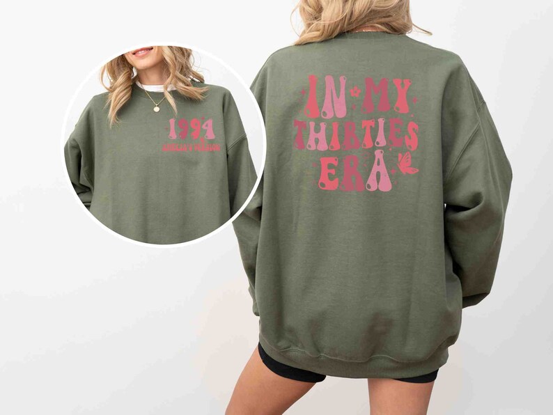 May include: A green sweatshirt with a pink and red graphic on the back that says "In My Thirties Era". The front of the sweatshirt has a pink and red graphic that says "1991" with the text "Golden Era" underneath.