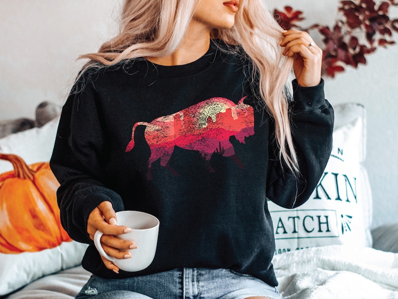 May include: A black sweatshirt with a graphic print of a red, orange, and yellow bison silhouette against a sunset background.