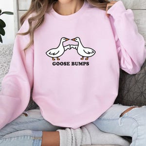 May include: A pink sweatshirt with a graphic of two geese facing each other with the text "Goose Bumps" underneath.