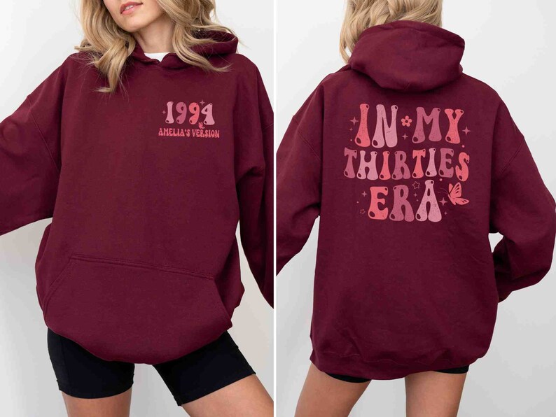 May include: Burgundy hoodie with a graphic on the back that says "In My Thirties Era" in a retro font with stars and a butterfly. The front of the hoodie has a graphic that says "1994 Amelia's Version".