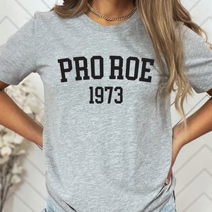 May include: A gray t-shirt with black text that reads "PRO ROE 1973".
