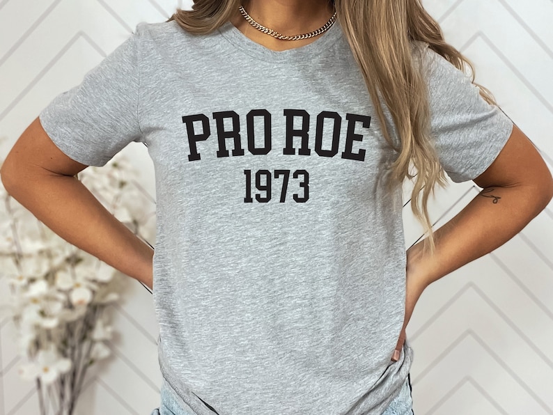 May include: A gray t-shirt with black text that reads "PRO ROE 1973".