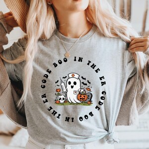 May include: A gray t-shirt with a black and white graphic of a ghost wearing a nurse's hat and holding a syringe and a pumpkin. The text around the ghost reads "Boo Code in the ER Code Boo".