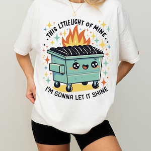 May include: White t-shirt with a graphic of a green dumpster with a smiling face and flames coming out of it. The text on the shirt reads "This little light of mine, I'm gonna let it shine."