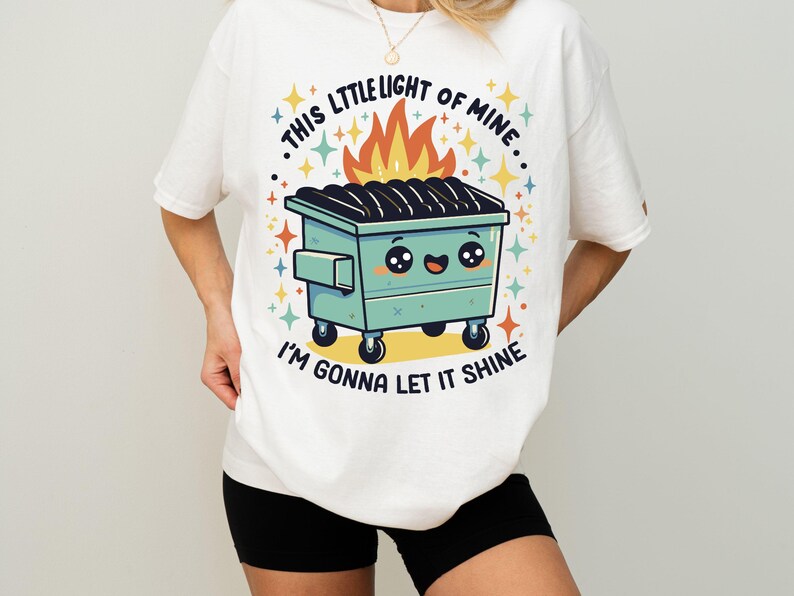 May include: White t-shirt with a graphic of a green dumpster with a smiling face and flames coming out of it. The text on the shirt reads "This little light of mine, I'm gonna let it shine."