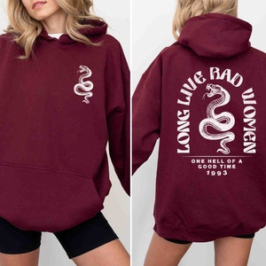 K&ouml;nnte beinhalten: Ein weinroter Hoodie mit einem wei&szlig;en Schlangen-Motiv auf der Vorderseite und einem wei&szlig;en Motiv auf der R&uuml;ckseite, das "Long Live Bad Women" mit einem Schlangen-Motiv und "One hell of a good time 1993" sagt.