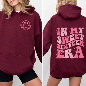 May include: Burgundy hoodie with a pink smiley face graphic on the front and "In My Sweet Sixteen Era" text on the back.
