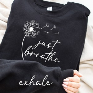 May include: Black sweatshirt with a white dandelion graphic and the text "just breathe exhale".