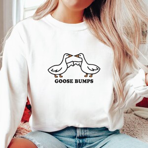 May include: White long-sleeve sweatshirt with a black and white illustration of two geese facing each other with the text "GOOSE BUMPS" underneath.