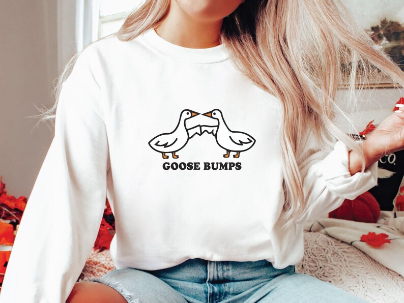 May include: White long-sleeve sweatshirt with a black and white illustration of two geese facing each other with the text "GOOSE BUMPS" underneath.