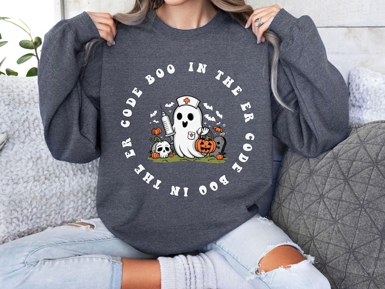May include: A dark gray sweatshirt with a white graphic of a ghost wearing a nurse's hat and holding a pumpkin. The text around the ghost reads "Boo in the ER Code the Boo in the ER Code".