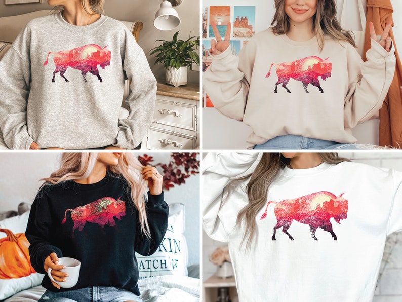 May include: Four different color sweatshirts featuring a silhouette of a bison with a sunset landscape inside the silhouette. The sweatshirts are available in grey, beige, black, and white.