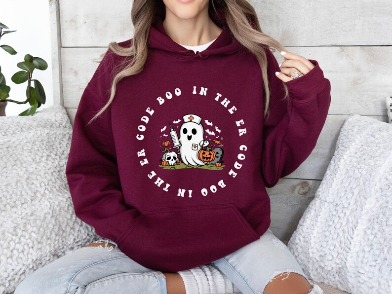 May include: A maroon hoodie with a white graphic of a ghost wearing a nurse's cap and holding a syringe. The text around the ghost reads "Boo in the ER Code the Boo in the ER Code".