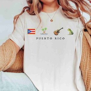 May include: White t-shirt with a Puerto Rican flag, palm trees, a guitar, and a frog. The text "PUERTO RICO" is printed below the images.
