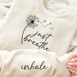 May include: A cream-colored sweatshirt with the text "just breathe inhale" and a black dandelion graphic.