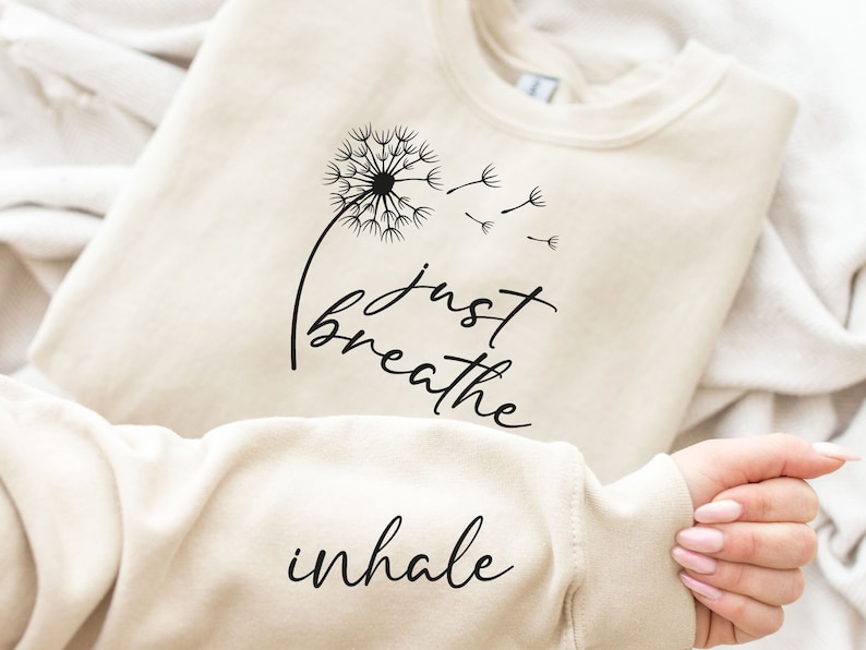 May include: A cream-colored sweatshirt with the text "just breathe inhale" and a black dandelion graphic.