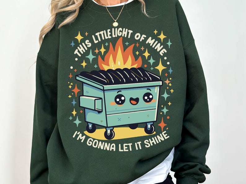 May include: A dark green sweatshirt with a cartoon image of a green dumpster with a smiling face and flames coming out of the top. The text "This little light of mine, I'm gonna let it shine" is printed on the sweatshirt.
