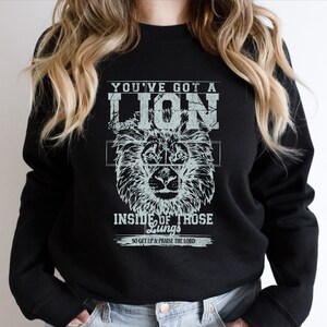 May include: Black sweatshirt with a white graphic print of a lion's head and the text "You've got a lion inside of those lungs, so get up & praise the Lord."