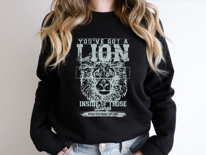May include: Black sweatshirt with a white graphic print of a lion's head and the text "You've got a lion inside of those lungs, so get up & praise the Lord."
