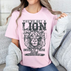 May include: Pink t-shirt with a black and white lion graphic and the text "You've got a lion inside of those lungs. So get up & praise the Lord."