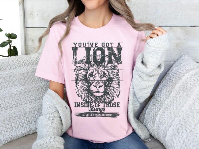 May include: Pink t-shirt with a black and white lion graphic and the text "You've got a lion inside of those lungs. So get up & praise the Lord."