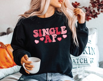 May include: Black sweatshirt with the text "SINGLE AF" in pink and red letters with pink hearts around the text.