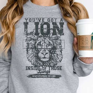 May include: Gray sweatshirt with a lion graphic and the text "You've got a lion inside of those lungs. So get up & praise the Lord."