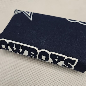Pu&ograve; includere: Un porta fazzoletti in tessuto blu scuro con stelle bianche e la parola "Cowboys" stampata su di esso.