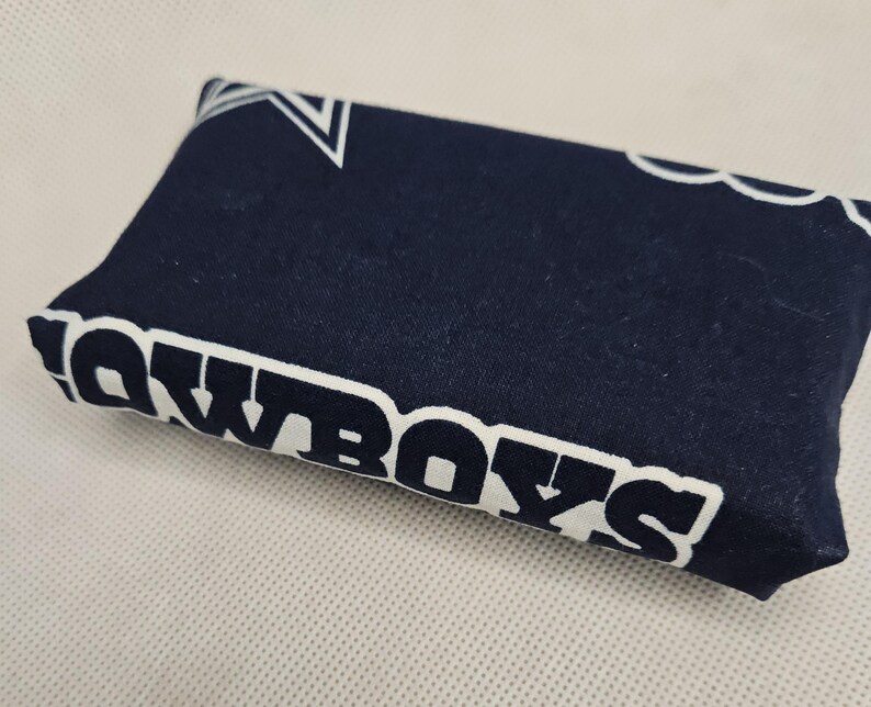Pu&ograve; includere: Un porta fazzoletti in tessuto blu scuro con stelle bianche e la parola "Cowboys" stampata su di esso.