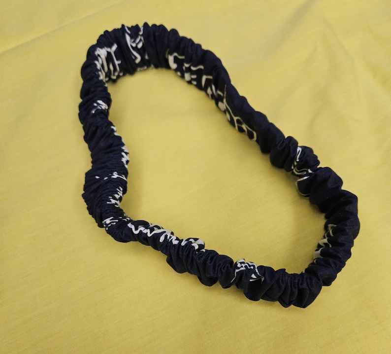 Pu&ograve; includere: Un cerchietto elastico blu navy con un motivo bianco.