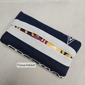 Pu&ograve; includere: Un porta fazzoletti a righe blu e bianche con la scritta "Tissue holder" stampata sul davanti.
