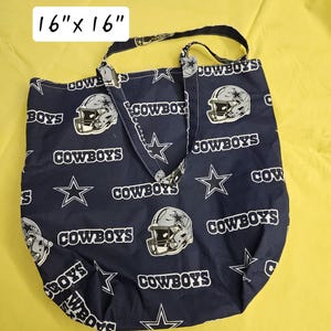 Pu&ograve; includere: Una borsa tote blu con un motivo a stella bianca e casco da football. La borsa ha due manici e dice "COWBOYS" ripetutamente. La borsa misura 16 pollici per 16 pollici.