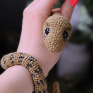 May include: A crocheted snake toy with brown and black yarn. The snake has a small, round head with black eyes and a curled tail.