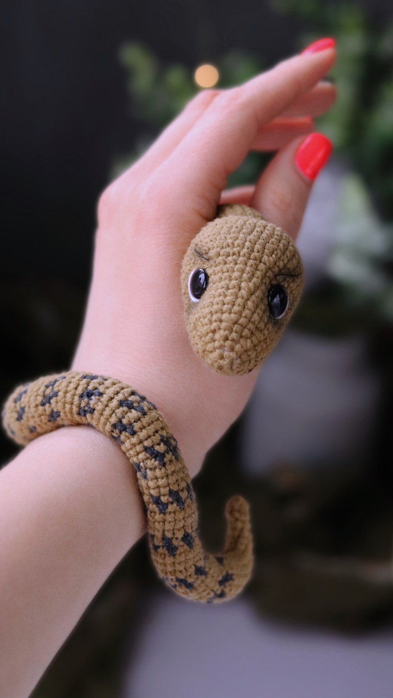 May include: A crocheted snake toy with brown and black yarn. The snake has a small, round head with black eyes and a curled tail.