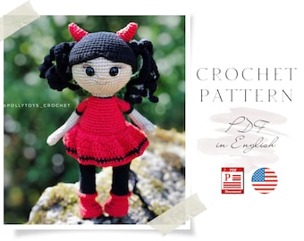 May include: Crochet pattern PDF in English for a red and black crocheted doll with horns, pigtails, and a dress. The doll is standing on a rock.