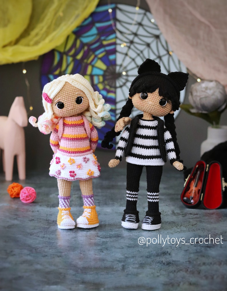 May include: Two crocheted dolls, one with blonde hair wearing a pink and orange striped shirt, a white skirt with pink flowers, and yellow sneakers, and the other with black hair wearing a black and white striped shirt, black pants with white stripes, and black sneakers. The dolls are standing on a gray surface. The text "@pollytoys_crochet" is at the bottom of the image.