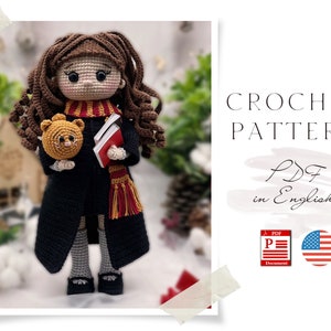 Könnte beinhalten: Häkelanleitung PDF in Englisch für eine Puppe mit braunen Haaren, einem rot-goldenen Schal, einem Buch und einer kleinen orangefarbenen Katze. Die Anleitung enthält ein US-Flaggen-Symbol.