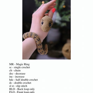 May include: A crocheted snake toy in brown and black with a light brown head and black eyes. The snake is wrapped around a person's wrist. The image includes a list of crochet abbreviations, such as MR for Magic Ring, sc for single crochet, ch for chain, dec for decrease, inc for increase, hdc for half double crochet, dc for double crochet, sl st for slip stitch, BLO for Back loop only, FLO for Front loop only, and (..) * for repeat instructions in brackets with the required number of times. The text at the bottom of the image reads "@pollytoys_crochet All rights reserved 6".