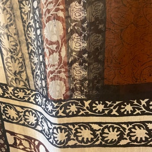 May include: Close-up of a sheer fabric with a repeating floral and geometric pattern. The design features vertical stripes in shades of brown, black, white, and gray. The fabric has a delicate, flowing appearance, suggesting it might be used for scarves or curtains.