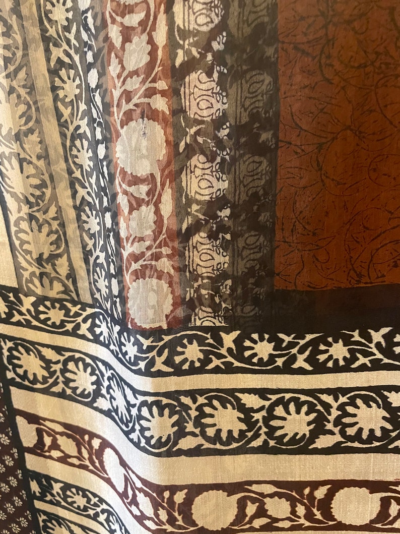 May include: Close-up of a sheer fabric with a repeating floral and geometric pattern. The design features vertical stripes in shades of brown, black, white, and gray. The fabric has a delicate, flowing appearance, suggesting it might be used for scarves or curtains.