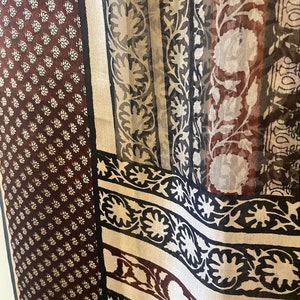 May include: A sheer fabric with a variety of patterns. The left side features a dark brown background with small white floral designs. The right side has vertical stripes with floral and geometric patterns in black, white, and brown.