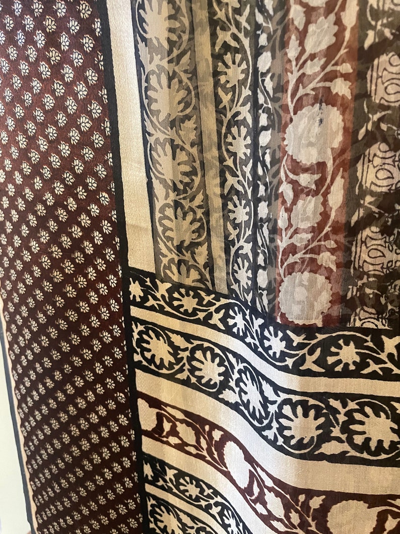 May include: A sheer fabric with a variety of patterns. The left side features a dark brown background with small white floral designs. The right side has vertical stripes with floral and geometric patterns in black, white, and brown.