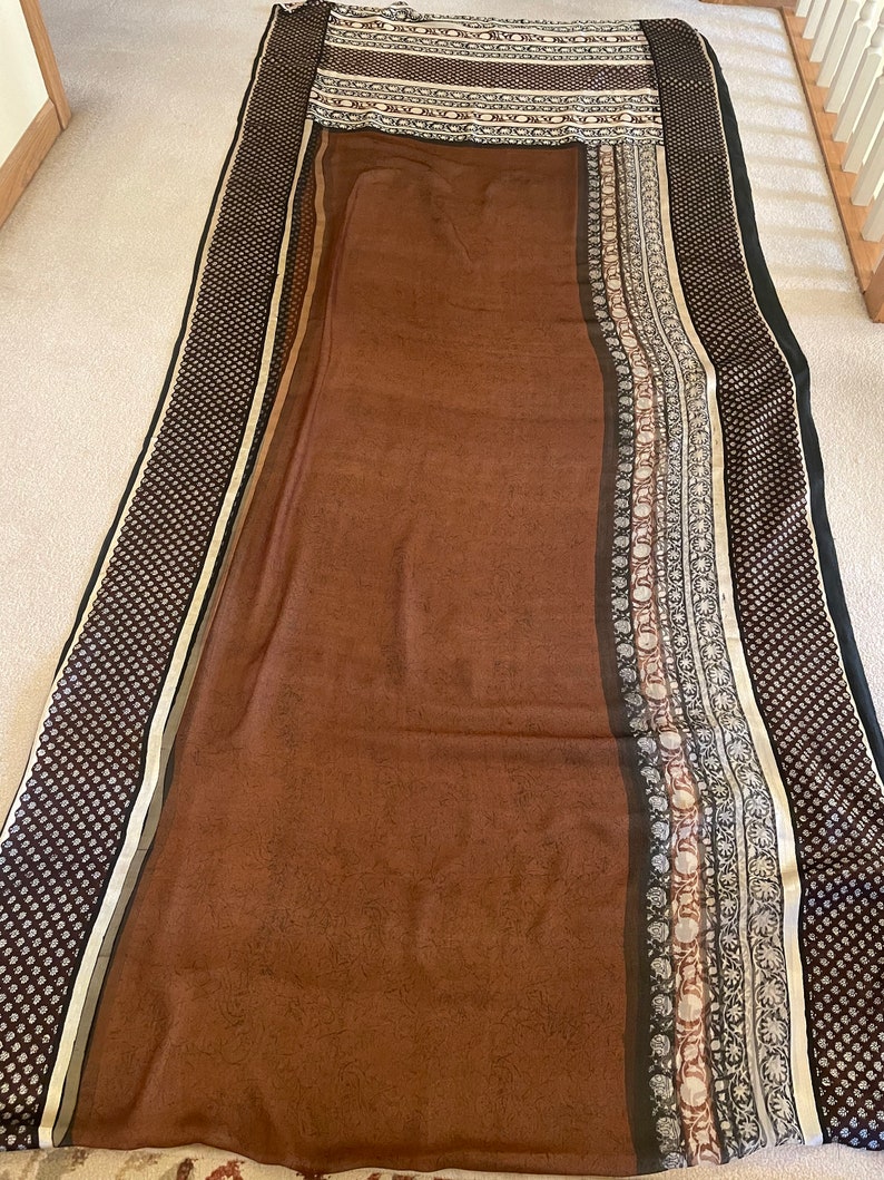 May include: A brown textile with a patterned border and a central field. The border features a repeating dot pattern in black and white, with a stripe of gold and cream. The central field is a solid brown color with a subtle pattern.