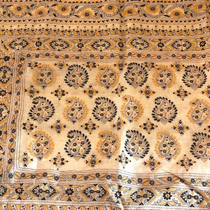 May include: A cream-colored textile featuring intricate hand-stitched embroidery in black and yellow thread. The fabric displays a repeating pattern of paisley motifs, floral elements, and geometric borders, all accented with fine running stitches.