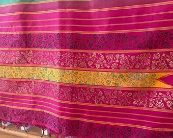 May include: A vibrant textile featuring a repeating pattern of horizontal stripes in shades of fuchsia and gold. Floral designs in gold and black adorn the fabric, with a yellow and green central band. The textile has a fringed edge.