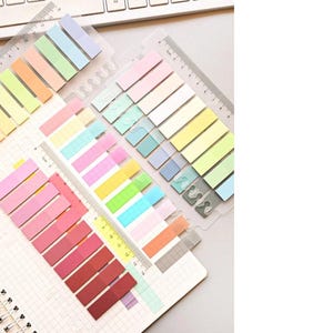 May include: A set of colourful sticky notes in a variety of pastel shades, including pink, blue, green, yellow, and orange. The notes are arranged in a clear plastic holder with a ruler on the side.
