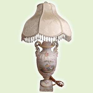 May include: A white porcelain lamp base with a floral design and a white lampshade with a fringe trim.